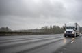 High cab big rig semi truck with dry van semi trailer driving on the wet highway road with storm raining weather at twilight Royalty Free Stock Photo