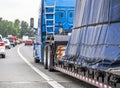 High cab blue big rig long haul semi truck transporting covered and fastened cargo on step down semi trailer driving on the Royalty Free Stock Photo