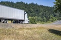 High cab long hauler big rig white semi truck transporting cargo in dry van semi trailer running on the winding summer road with Royalty Free Stock Photo