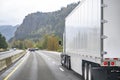 High cab long hauler white big rig semi truck transporting cargo in dry van semi trailer running on the wide highway road in Royalty Free Stock Photo