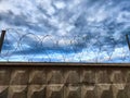 High concrete wall and fence with barbed wire on background of sky with clouds and small piece of blue sky. Protected Royalty Free Stock Photo