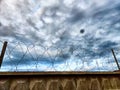 High concrete wall and fence with barbed wire on background of sky with clouds and small piece of blue sky. Protected Royalty Free Stock Photo