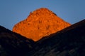 High desert peak illuminated by the golden light of sunset above a ridge that is in shadow