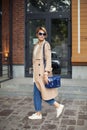 High Fashion Clothing. Beautiful Woman Wearing Fashionable Spring Or Fall Clothes beige trench coat, blue bag, jeans, Royalty Free Stock Photo