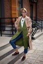 High Fashion Clothing. Beautiful Woman Wearing Fashionable Spring Or Fall Clothes beige trench coat, long green sweater, Royalty Free Stock Photo