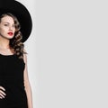 High fashion outdoor full length portrait of elegant woman in black hat and dress standing behind white pillar. Royalty Free Stock Photo