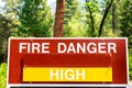 High fire danger sign informs the public that wildfires are likely. Green forest background Royalty Free Stock Photo