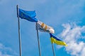 High flagpoles with flags of states developing under the gusts of wind against the background of a light blue sky with