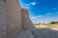 High fortress walls with crenellations lead to a corner tower against a clear sky, near modern buildings Royalty Free Stock Photo