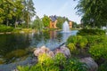 High fountain in the middle of the lake on the background of a wooden mansion, surrounded by tall green trees under a Royalty Free Stock Photo