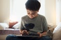 High key portrait happy young boy sitting on sofa playing game on tablet, School kid doing online homework on digital pad. Child Royalty Free Stock Photo