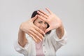 High key portrait of a young smiling woman looking at the camera through her hand framing. Selective focus on hands Royalty Free Stock Photo