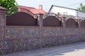 High long wall of a private fence made of gray stones and brown metal