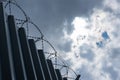 High metal corrugated wall with barbed wire and gray sky Royalty Free Stock Photo