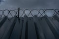 High metal corrugated wall with barbed wire and gray sky Royalty Free Stock Photo