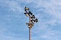 High metal pole with multiple light reflectors and security camera connected with electrical wires on cloudy blue sky back