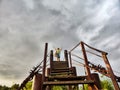 High, old, rusty iron staircase and tiny statue of girl or woman at the top against backdrop of gray, gloomy, thunderous