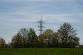 A high power pole in front of another in the foreground a field and a farmer doing his work with the tractor