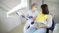 High-qualified dentist shows the young female patient an X-ray of the teeth in the dental chair at modern clinic.