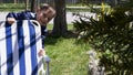 High quality close-up of a boy peeps out of white and blue striped chair outside wearing rain coat during summer time. Happy kid