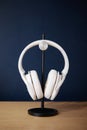 White wireless head large headphones stand on a wooden table on a black stand on a blue background side view