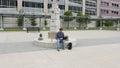 High quality picture of a young man who is sitting on a concrete monument base outside of train and bus station and holding laptop