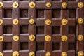 High res antique dark brown polished wooden door with geometric symmetrical square and golden rosettes decoration close up