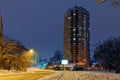 High-rise apartment building against the background of a city street in a winter city evening park covered with snow against a