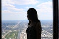 high rise building window silhouette of a young woman looking out the window at a suburban metropolis langscape with day blue sky Royalty Free Stock Photo