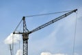 High-rise industrial tower crane with rusty cabin against blue sky with fluffy clouds. Construction site. Copy space. Royalty Free Stock Photo