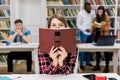 High school, education and people concept. Pretty student girl hiding her face over open book on modern college library Royalty Free Stock Photo
