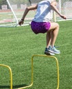 Teenage girl in purple shorts jumping over yellow hurdles