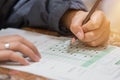 High school or university student hands taking exams, writing examination on paper answer sheet optical form of standardized test