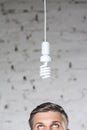 High section of thoughtful mature businessman looking at energy efficient lightbulb hanging against brick wall at office Royalty Free Stock Photo