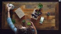 High shot of female designer organising things on wooden table getting ready to take flat lay pictures. Green plants