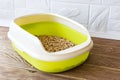 High sided cat litter tray with wooden pellets on a brown wooden floor. New green cat box near the wall. Toilet for domestic pets Royalty Free Stock Photo