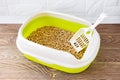 High sided cat litter tray with wooden pellets and scoop on a brown wooden floor. New green cat box near the wall. Toilet for Royalty Free Stock Photo