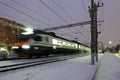 High-speed passenger electric train at night. A beam of train spotlight illuminates the falling snow