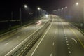 High-speed suburban highway in the light of streetlights. There are yellow and white markings on the asphalt. There are signs on