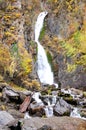 A high, stormy waterfall flows from the mountain in a rapid stream into the autumn forest Royalty Free Stock Photo
