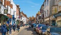 High street of Old Rye town with periodic buildings, lots of people and cars parked on side.