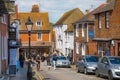 High street of Old Rye town with periodic buildings, lots of people and cars parked on side.