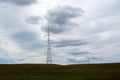 High tension electricity poles and cables over green grass field and gray cloudy sky in the countryside Royalty Free Stock Photo