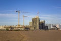 High tower cranes near the concrete structures under construction of skyscrapers against the backdrop of modern high-rise