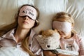 High view of Caucasian mother and daughter, stuffed teddy bear toy sleeping in blindfolds on the bed in bedroom at home. Relax, Royalty Free Stock Photo