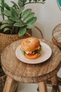 High view of a Double cheeseburger stacked high, cheese dripping, sitting on a wooden table, and behind there are herbs