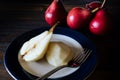 High view of a halved, unpeeled red battler pear on a plate and other pears on the table. Dark background. Organic and natural