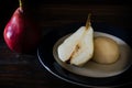 High view of a halved, unpeeled red battler pear on a plate and other pears on the table. Dark background. Organic and natural