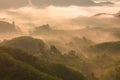 High views with views of mountains and fog interspersed among lush green forests at sunrise, golden light, sky and colorful clouds