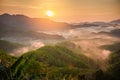 High views with views of mountains and fog interspersed among lush green forests at sunrise, golden light, sky and colorful clouds